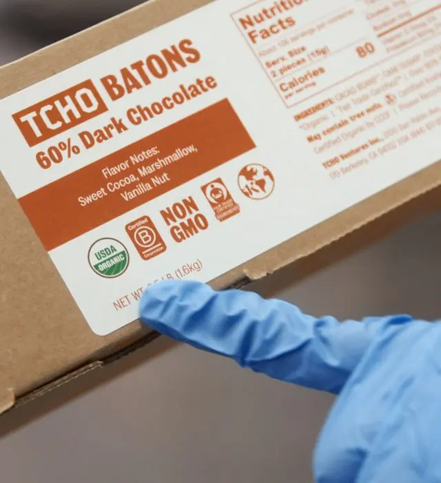 Gloved hand pointing to certification seals on an organic dark chocolate case label.