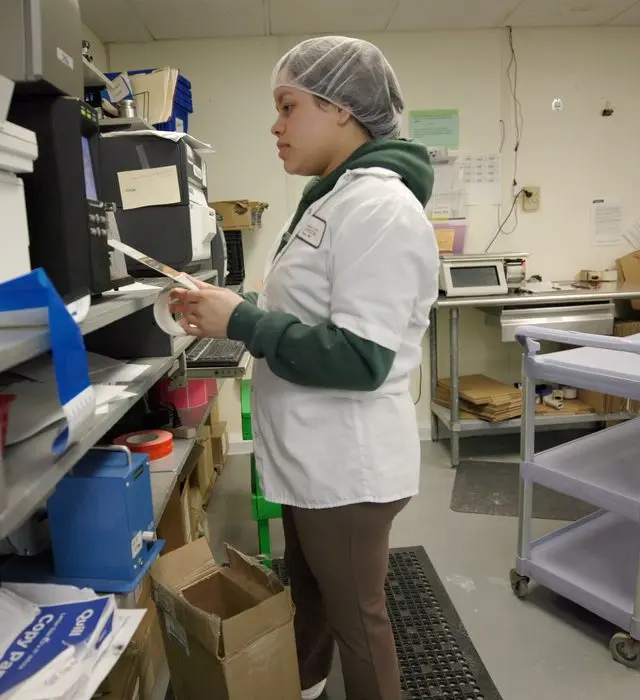 Food production worker in a hair net reviewing an ingredient label at a workstation.
