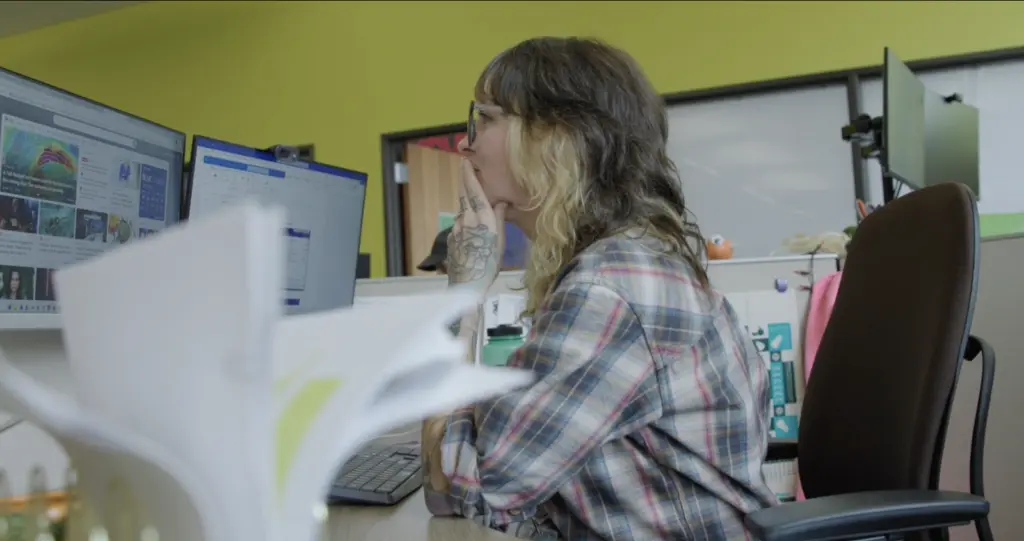 Woman at office desk reviewing monitors with website interface and data.