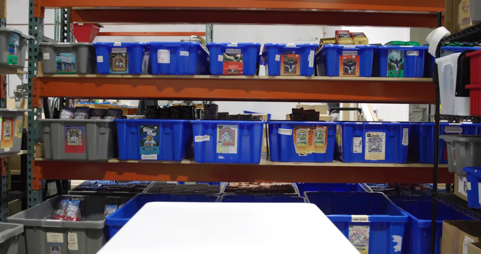 Labeled blue and grey storage totes of packaged coffee on warehouse racking