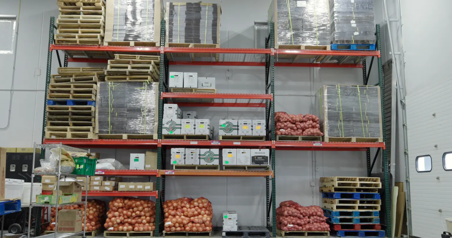 Warehouse racking holding pallets of onions, produce cartons and stacked wooden pallets in a storage room