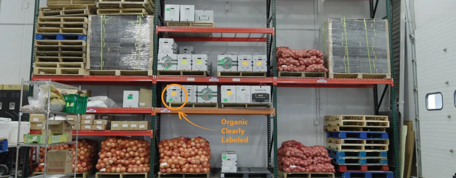 Warehouse racks holding pallets, produce cartons and onions, with an arrow identifying a clearly labeled organic carton