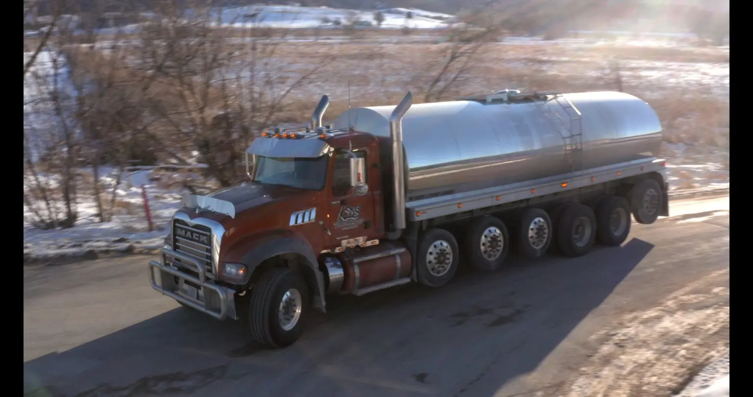 Tanker truck pulling a polished stainless steel bulk trailer along a snowy rural road