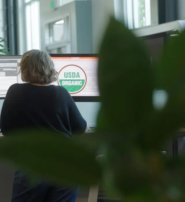 A person working at a computer with the USDA Organic seal displayed on screen.