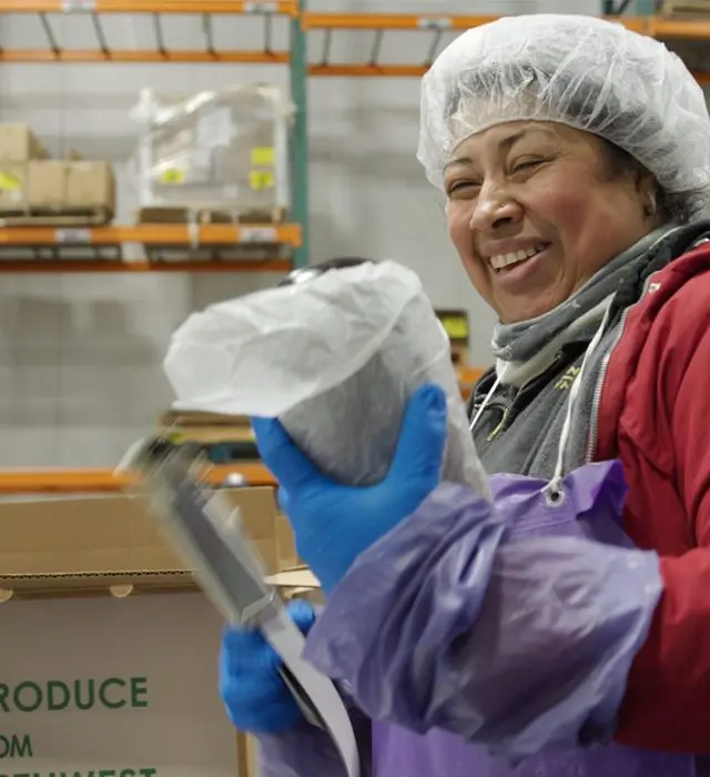 A smiling food production worker in a hairnet and protective clothing handling ingredients.