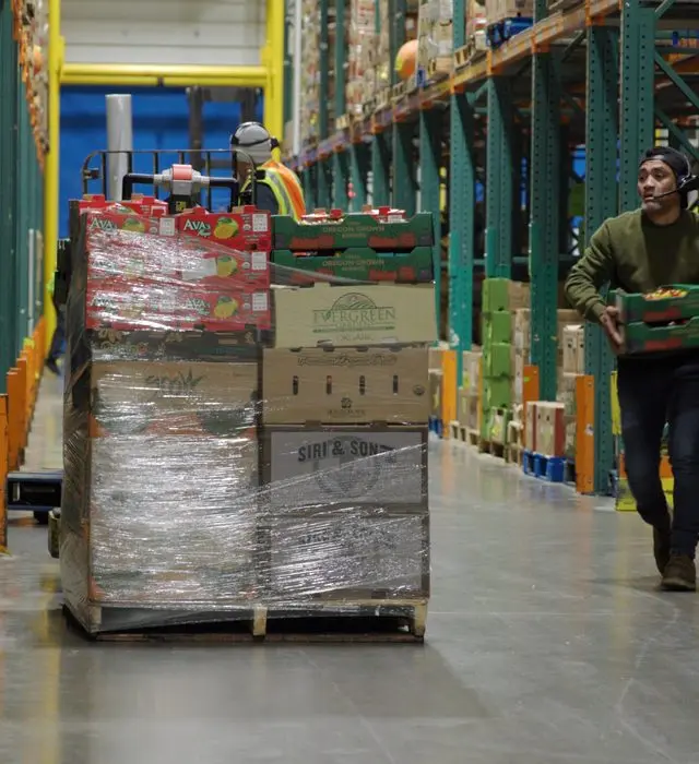 Workers moving a pallet through a warehouse aisle.